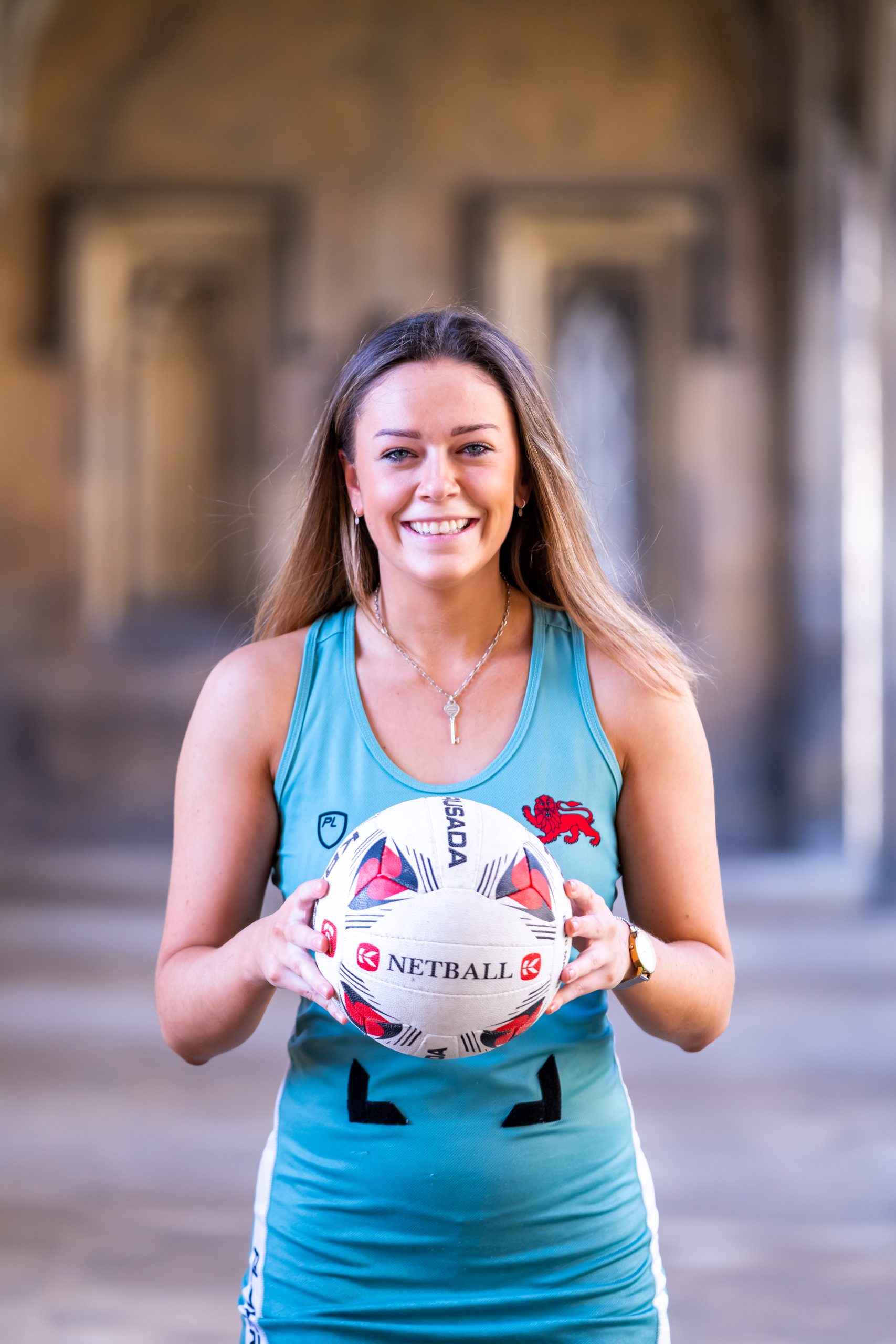 The CULNC captain stands smiling in her netball dress, holding a netball in front of her